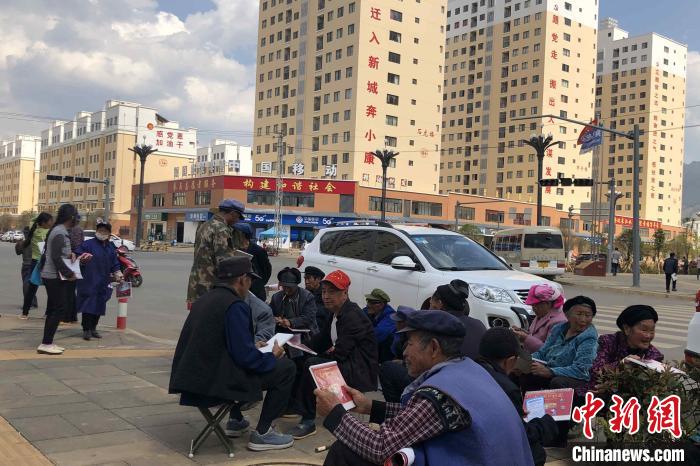 圖為會澤縣城易地扶貧搬遷安置點內，老人們聚在廣場上聊天，身后是他們的新家。　繆超 攝